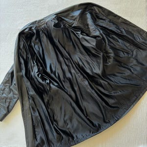 May include: A black leather jacket, open to reveal a black satin lining. The jacket is laid out on a white surface, showcasing the interior construction and design. The leather appears worn, adding character.
