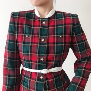 Puede incluir: Una chaqueta de cuadros rojos, verdes y blancos con botones dorados y un cintur&oacute;n blanco. La chaqueta tiene un cuello alto y mangas largas.