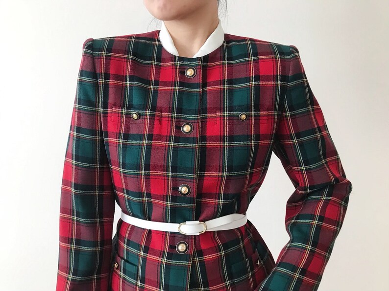 Puede incluir: Una chaqueta de cuadros rojos, verdes y blancos con botones dorados y un cintur&oacute;n blanco. La chaqueta tiene un cuello alto y mangas largas.