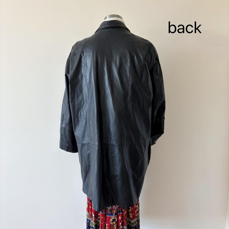 May include: Back view of a black leather jacket. The jacket has a collared neckline and long sleeves. The text "back" is printed in black on the upper right side of the image. The jacket is worn over a colorful patterned skirt.