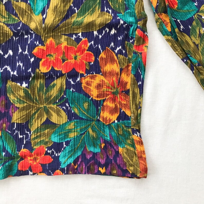 May include: A close-up of a fabric with a tropical print. The fabric features a dark blue background with green, orange, and red flowers and leaves.