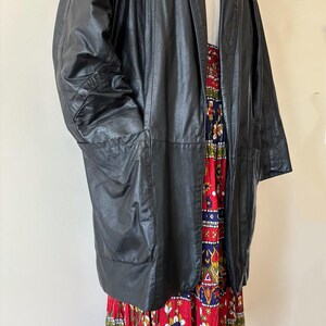 May include: A black leather jacket with large pockets. The jacket is open, revealing a colorful floral print dress. The dress features red, blue, and white floral patterns. The jacket appears to be vintage.