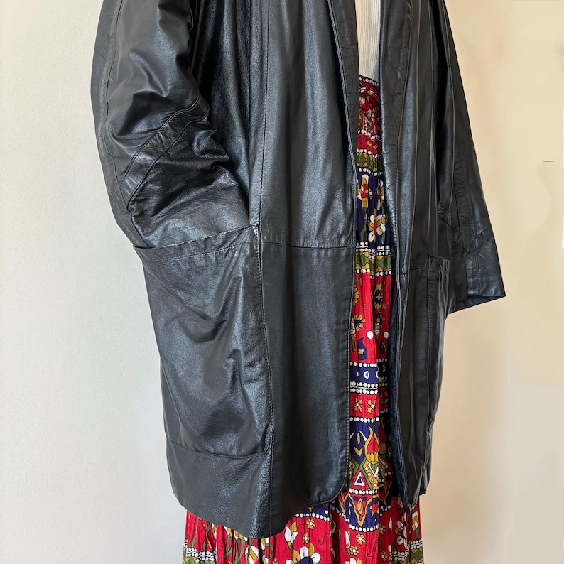 May include: A black leather jacket with large pockets. The jacket is open, revealing a colorful floral print dress. The dress features red, blue, and white floral patterns. The jacket appears to be vintage.
