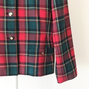 Puede incluir: Una chaqueta de cuadros rojos, verdes y blancos con botones dorados. La chaqueta tiene un bolsillo en el lado izquierdo.