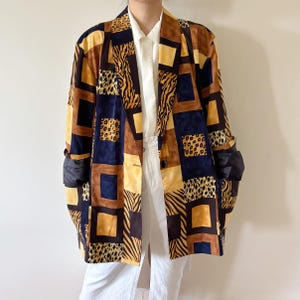 May include: A patchwork blazer in shades of brown, yellow, and navy blue. The blazer features a mix of animal print patterns, including leopard and zebra stripes. It has a classic tailored design with a button closure and long sleeves.