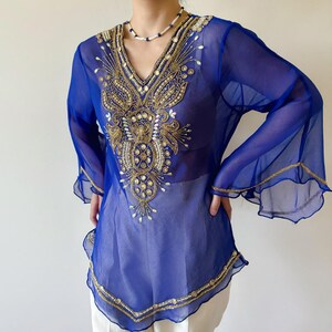 May include: A sheer blue top with a gold and pearl beaded design. The top has a V-neck and long sleeves with bell bottoms.