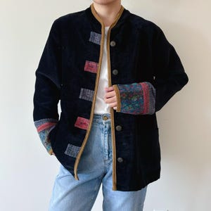 May include: A black velvet jacket with brown trim and colourful embroidered details on the cuffs. The jacket has a mandarin collar and a button closure.