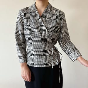 May include: A black and white houndstooth wrap blouse with a long sleeve and a tie at the waist.