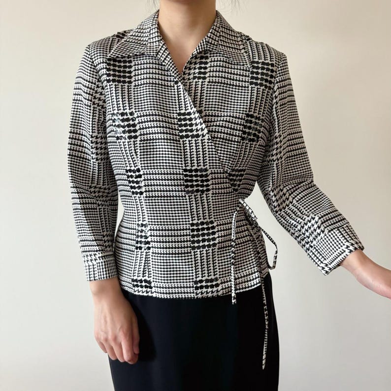 May include: A black and white houndstooth wrap blouse with a long sleeve and a tie at the waist.