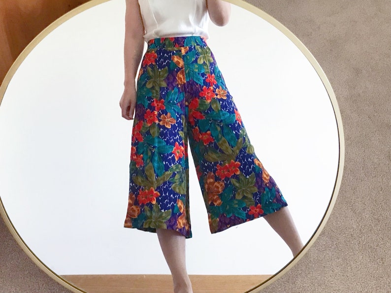 May include: High-waisted wide-leg cropped pants with a colorful floral print featuring red, orange, yellow, green, blue, and purple flowers on a dark blue background.