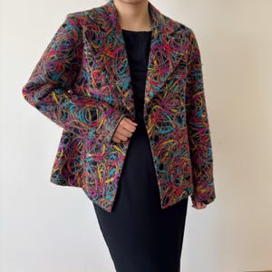 May include: A multi-colored blazer with a black base, featuring a vibrant pattern of interwoven lines in shades of red, yellow, blue, and purple. The blazer has a classic lapel and button closure.