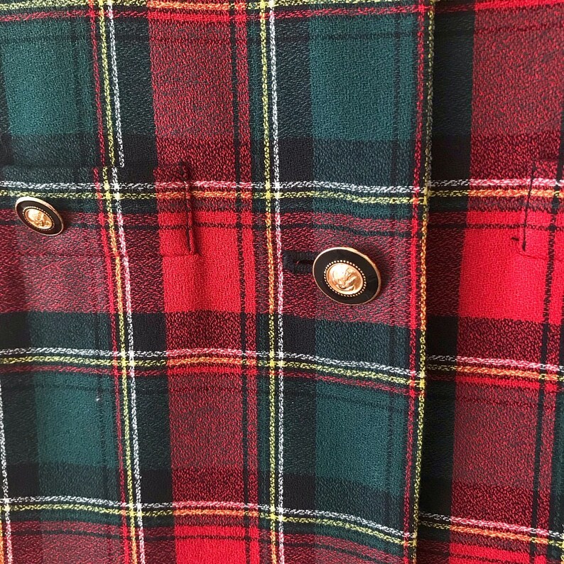 Puede incluir: Tela de cuadros rojos, verdes y blancos con dos botones dorados. Los botones tienen un centro negro y un dise&ntilde;o en relieve.