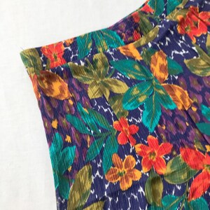 May include: A close-up of a fabric with a vibrant floral print. The fabric features a mix of orange, red, green, and blue flowers on a dark blue background.