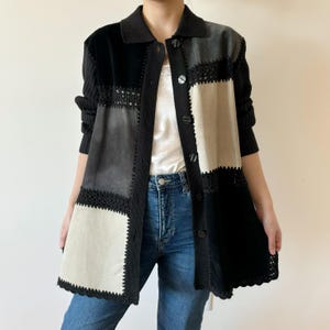 May include: A black and white patchwork cardigan with a crocheted trim. The cardigan has a button-up front and long sleeves.