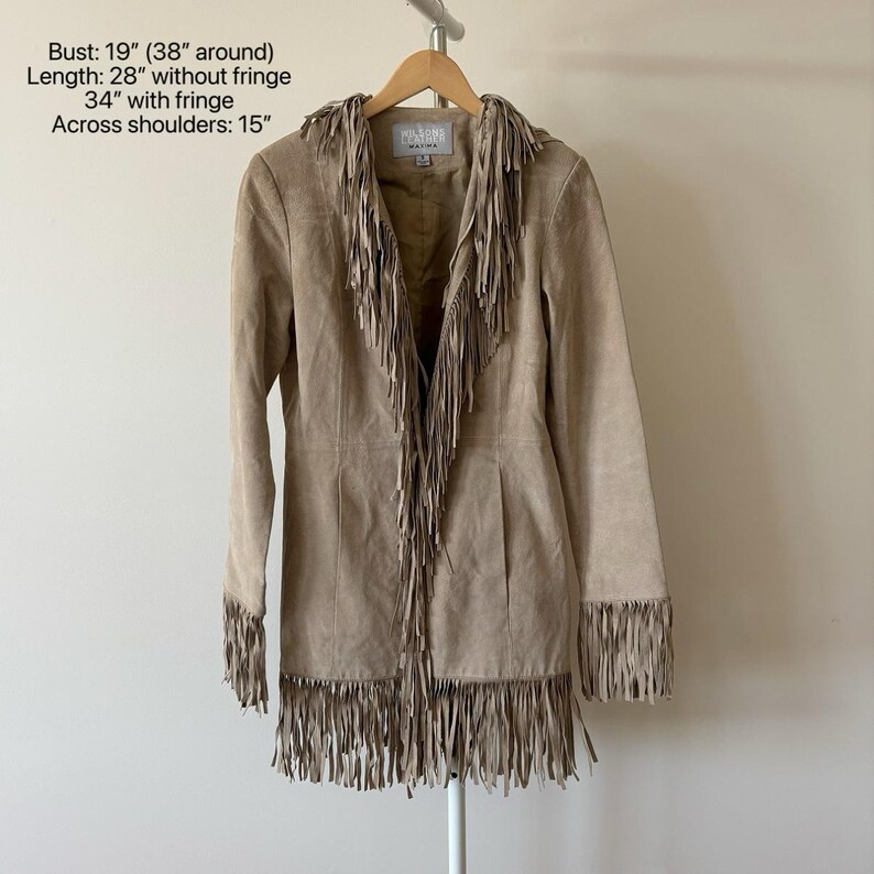 May include: A tan suede jacket with long sleeves and fringe detailing. The jacket has fringe along the collar, front, and sleeves. Bust: 19 inches (38 inches around), Length: 28 inches without fringe, 34 inches with fringe, Across shoulders: 15 inches.