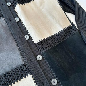 May include: A black cardigan with a patchwork design featuring different textures and colors. The cardigan has a button closure and a crocheted trim.