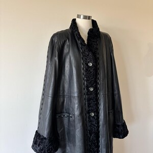 May include: A black leather coat featuring a textured black fur-like trim along the collar, front placket, and sleeve cuffs. The coat includes three circular buttons down the center front and decorative woven leather detailing along the seams.