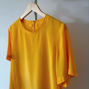 Puede incluir: Una blusa de manga corta de color amarillo brillante con cuello redondo.