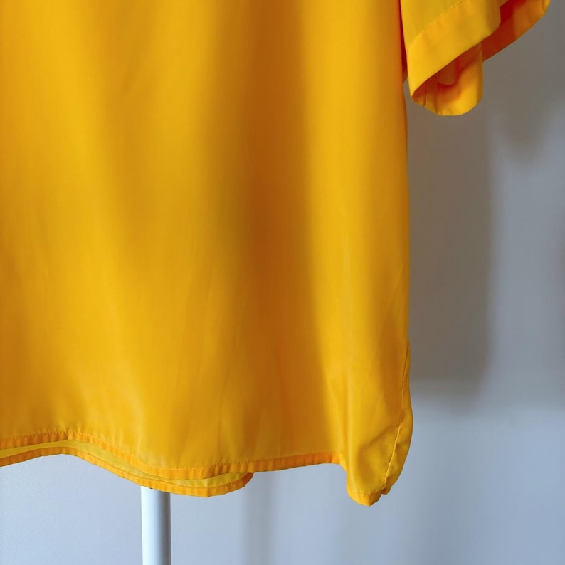 Puede incluir: Una camisa de manga corta de color amarillo brillante con una textura suave y sedosa.
