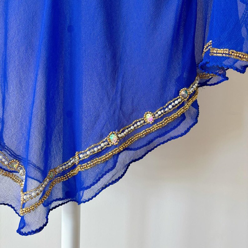 May include: A royal blue sheer fabric with a gold and white beaded trim. The trim features iridescent rhinestones.