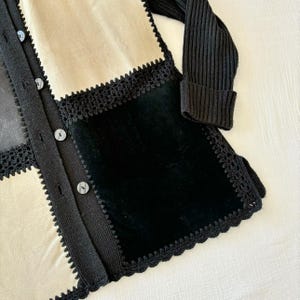 May include: A black and cream cardigan with a crocheted trim and a black velvet panel. The cardigan has a button closure.