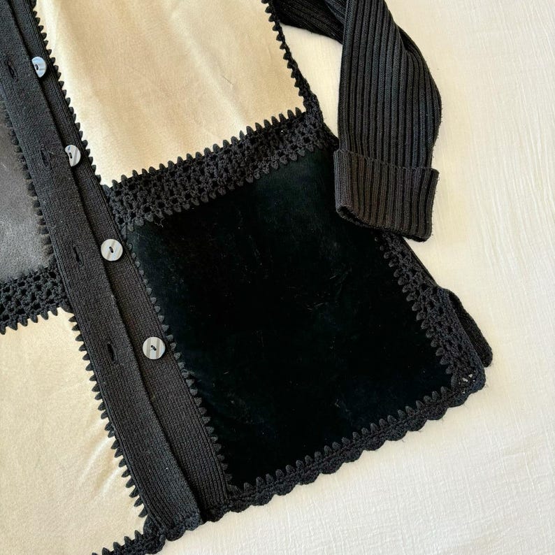 May include: A black and cream cardigan with a crocheted trim and a black velvet panel. The cardigan has a button closure.