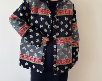 May include: A patterned jacket in black, gray, red, and gold. The jacket features a repeating floral design and is buttoned up. The jacket has a collared neckline and two pockets.