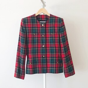 Puede incluir: Una chaqueta de cuadros rojos, verdes y negros con botones dorados. La chaqueta tiene un cuello mandar&iacute;n y cierre de botones en la parte delantera.