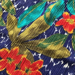 May include: A close-up of a blue fabric with a tropical print featuring red, yellow, green, and turquoise flowers and leaves.