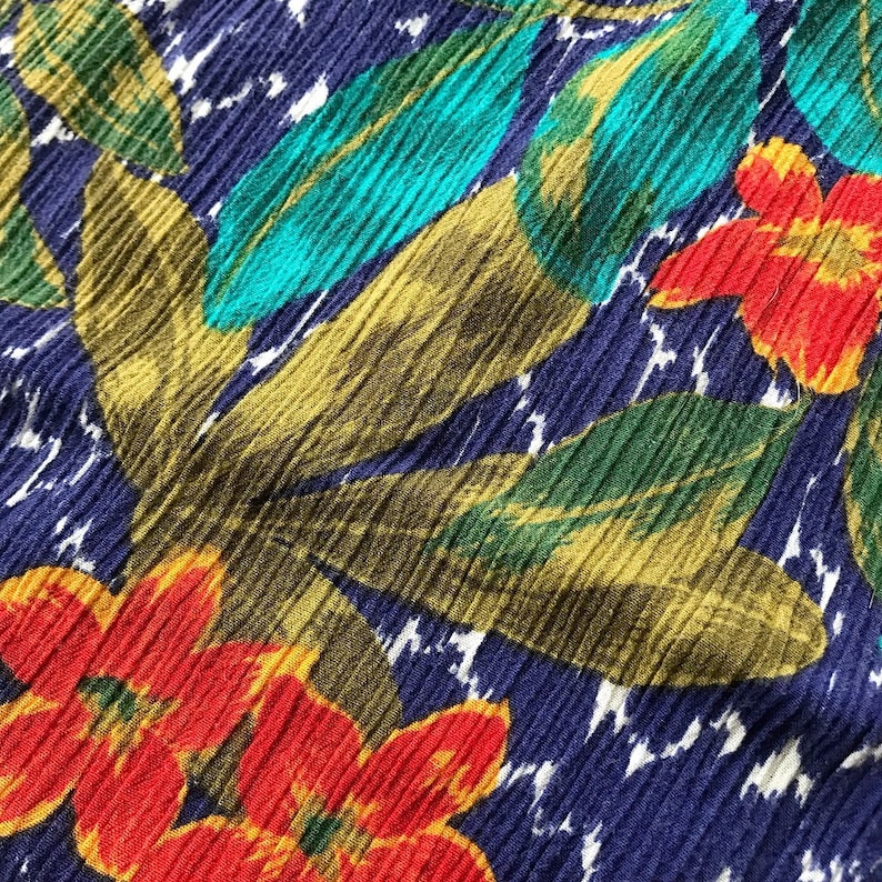 May include: A close-up of a blue fabric with a tropical print featuring red, yellow, green, and turquoise flowers and leaves.