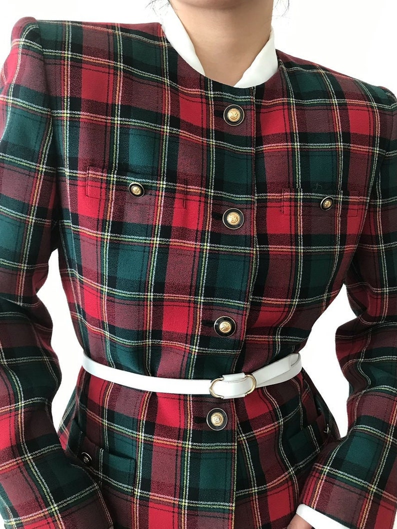 Puede incluir: Una chaqueta de cuadros rojos, verdes y blancos con botones dorados y un cintur&oacute;n blanco.