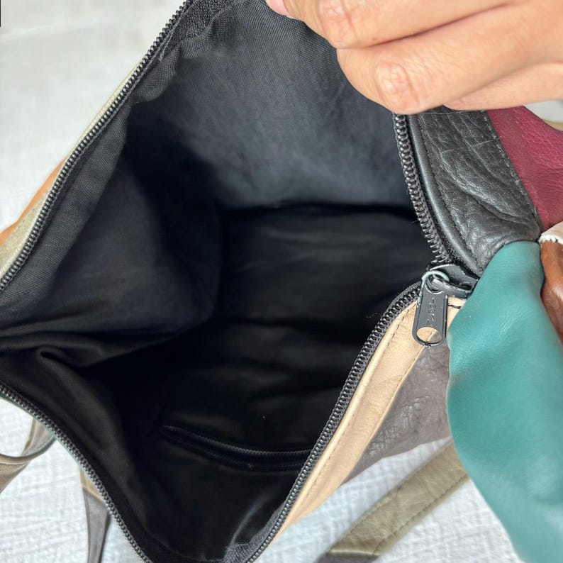 May include: Open view of a multi-colored leather shoulder bag. The bag features a black interior and a zipper closure. The exterior leather is a patchwork of colors including tan, green, burgundy, and black.