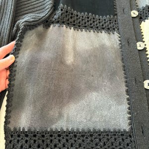 May include: Black cardigan sweater with a crocheted trim and a suede patch on the front. The cardigan has a button closure.