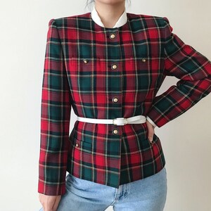 Puede incluir: Una chaqueta de cuadros rojos, verdes y blancos con un cintur&oacute;n blanco y botones dorados. La chaqueta tiene un cuello mandar&iacute;n y una longitud recortada.
