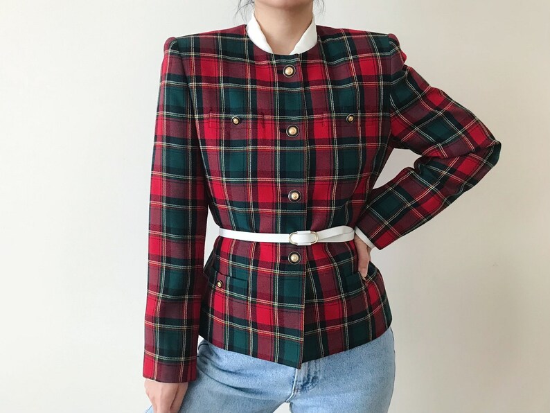 Puede incluir: Una chaqueta de cuadros rojos, verdes y blancos con un cintur&oacute;n blanco y botones dorados. La chaqueta tiene un cuello mandar&iacute;n y una longitud recortada.