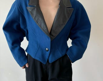 May include: A cropped blue blazer with a black leather collar. The blazer has a single button closure and long sleeves.