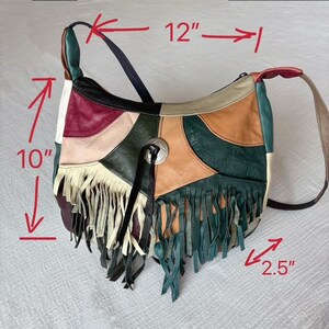 May include: A patchwork leather shoulder bag with a 10-inch height and 12-inch width. The bag features a variety of colors, including green, tan, burgundy, and black, with a fringe detail at the bottom. A silver-tone metal button adorns the front.