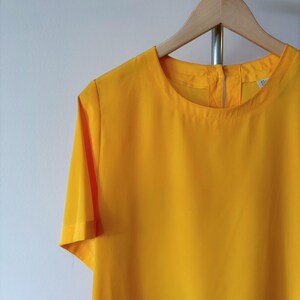 Puede incluir: Una blusa amarilla de manga corta con cuello redondo.