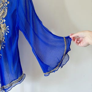 May include: A royal blue sheer top with gold embroidery and a ruffled trim. The top has a loose fit and three-quarter sleeves.