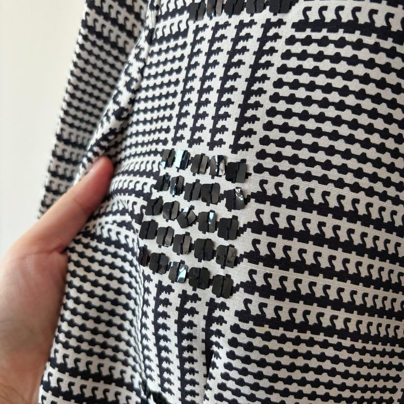 May include: Black and white patterned fabric with a black sequin design. The fabric has a geometric pattern.
