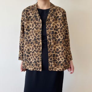 May include: A long-sleeved, open-front jacket with a brown and tan giraffe print. The jacket has a collared neckline and is worn over a black dress. The overall style is vintage and suitable for a variety of occasions.