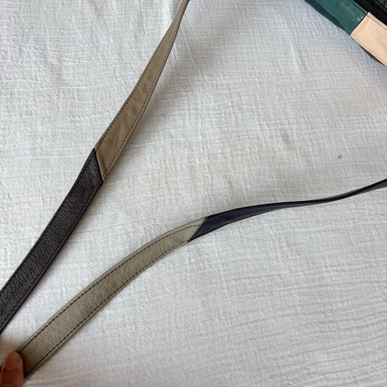 May include: Close-up of two leather bag straps. One strap is dark brown and tan, the other is black and tan. The straps are stitched together with a contrasting thread. The background is a white, textured surface.