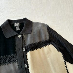 May include: Black, gray, and beige cardigan with a crocheted trim. The cardigan has a collar and button closure. The label reads "Designers Studio Originals".