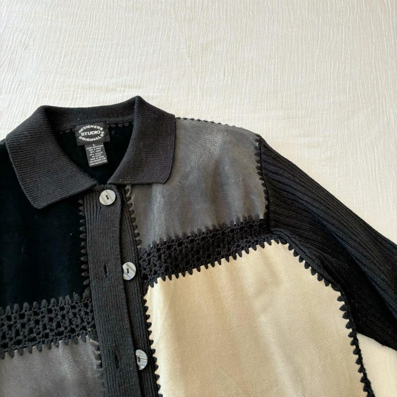 May include: Black, gray, and beige cardigan with a crocheted trim. The cardigan has a collar and button closure. The label reads "Designers Studio Originals".