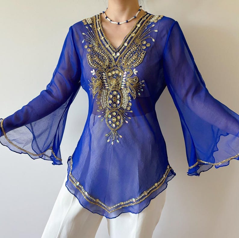 May include: A sheer blue top with long bell sleeves and a V-neckline. The top is embellished with gold and silver beading and sequins in a floral pattern.