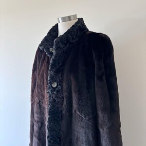 May include: A dark brown coat with a textured, curly black fur collar and front placket. The coat features a smooth, short-pile fur body with a scalloped hem design along the front panels and two visible round buttons along the center closure.