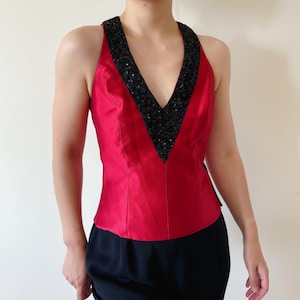 May include: A red satin halter top with a black beaded neckline. The top has a fitted bodice and a v-neckline.