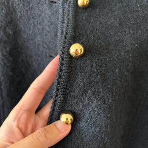 Puede incluir: Primer plano de un c&aacute;rdigan de punto gris oscuro con tres botones dorados brillantes. Los botones son redondos y reflejan la luz. El c&aacute;rdigan tiene un aspecto texturizado.