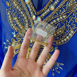May include: A blue sheer top with gold and white beading in a floral pattern. A small bag of gold beads is included.