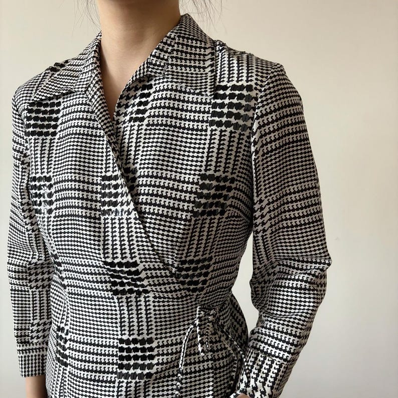 May include: A black and white checkered wrap dress with a long sleeve and a tie at the waist.